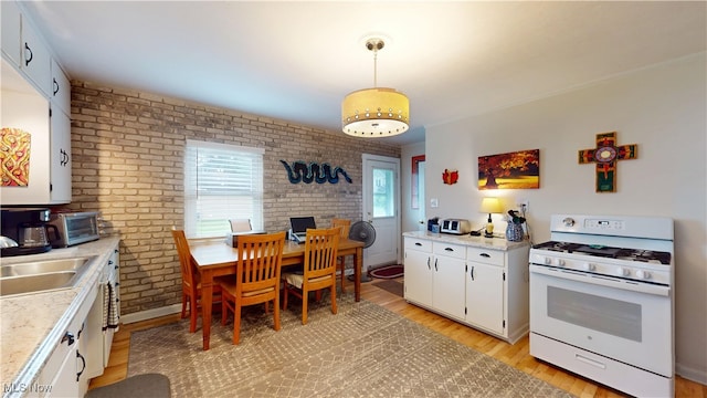 500 Elm St, Belpre, OH 45714 - kitchen featuring white gas range oven, brick wall, light wood finished floors, light countertops, and white cabinetry