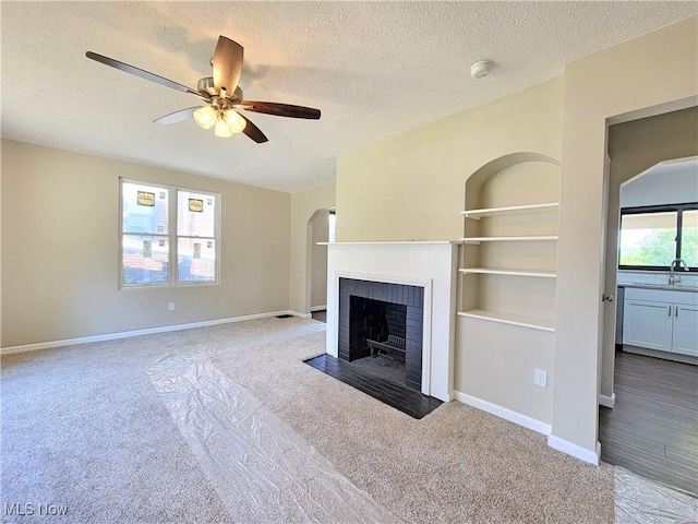 1006 Jackson Ave, Parkersburg, WV 26101 - unfurnished living room with carpet floors, a textured ceiling, a fireplace with flush hearth, a ceiling fan, and arched walkways