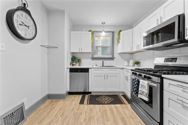 2602 Fletcher Ave NE, Canton, OH 44705 - kitchen with stainless steel appliances, white cabinetry, decorative backsplash, light wood finished floors, and light countertops