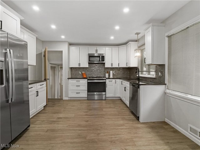 5265 Bellview St, Maple Heights, OH 44137 - kitchen featuring appliances with stainless steel finishes, dark countertops, tasteful backsplash, white cabinetry, and light wood-style flooring