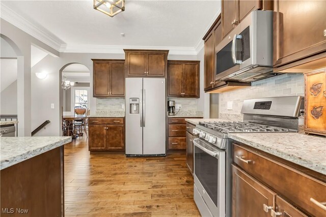 12110 Cora Ct, Concord, OH 44077 - kitchen with stainless steel appliances, arched walkways, light wood-style floors, ornamental molding, and tasteful backsplash