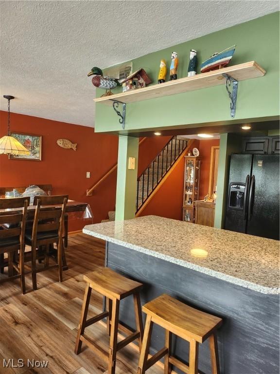 3545 Malley Ave, Coventry Township, OH 44319 - kitchen with black refrigerator with ice dispenser, a textured ceiling, wood finished floors, a kitchen breakfast bar, and light stone counters
