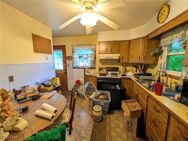 7567 Inland Dr, Olmsted Falls, OH 44138 - kitchen with under cabinet range hood, range with gas stovetop, brown cabinets, ceiling fan, and wainscoting