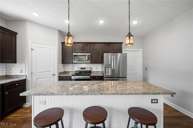 13176 Barrington Dr, Grafton, OH 44044 - kitchen featuring stainless steel appliances, dark brown cabinets, dark wood-style flooring, backsplash, and a breakfast bar