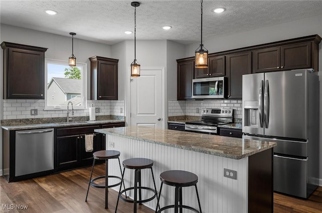 13176 Barrington Dr, Grafton, OH 44044 - kitchen featuring appliances with stainless steel finishes, dark brown cabinets, a textured ceiling, a kitchen bar, and dark stone countertops