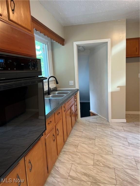 1820 E 47th St, Ashtabula, OH 44004 - kitchen with black oven, brown cabinets, a textured ceiling, dark countertops, and light marble finish flooring