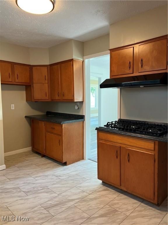 1820 E 47th St, Ashtabula, OH 44004 - kitchen with under cabinet range hood, black gas stovetop, brown cabinetry, a textured ceiling, and dark countertops