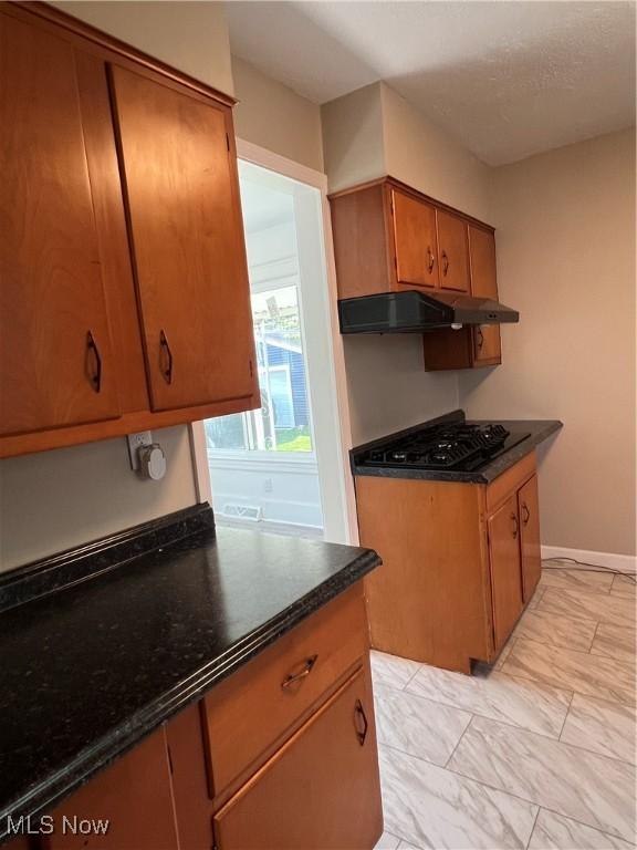 1820 E 47th St, Ashtabula, OH 44004 - kitchen with black gas stovetop, under cabinet range hood, dark countertops, brown cabinets, and light marble finish floors
