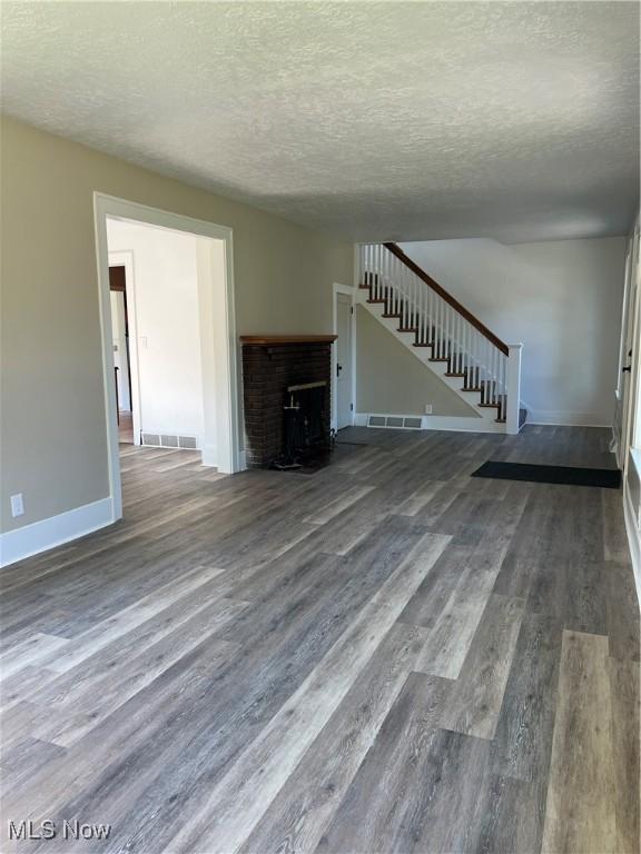 1820 E 47th St, Ashtabula, OH 44004 - unfurnished living room with stairway, wood finished floors, a textured ceiling, and a brick fireplace