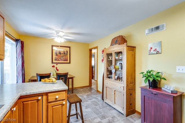 2207 Robinhood Dr, Wooster, OH 44691 - kitchen featuring stone finish floors, ceiling fan, light countertops, brown cabinets, and a breakfast bar area