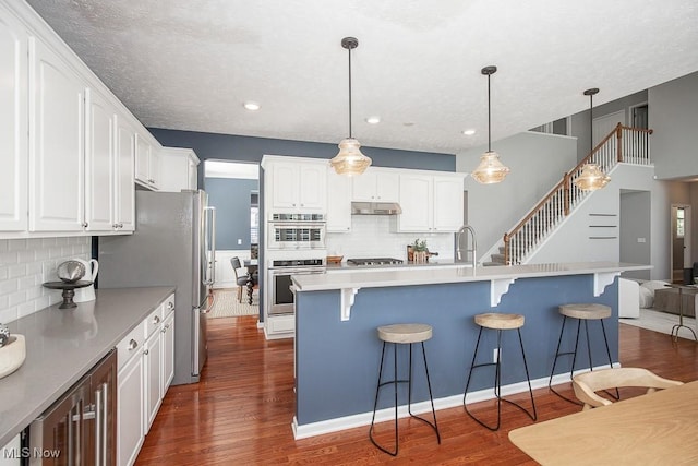 31008 Logan Ct, Westlake, OH 44145 - kitchen with appliances with stainless steel finishes, dark wood-style flooring, white cabinetry, decorative backsplash, and a breakfast bar area