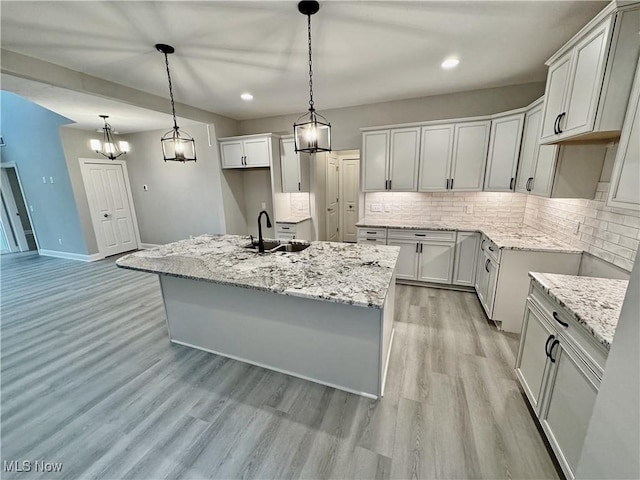 32054 Tuscan Ln Unit L-2, Avon Lake, OH 44012 - kitchen with backsplash, light wood-style flooring, recessed lighting, light stone countertops, and a center island with sink