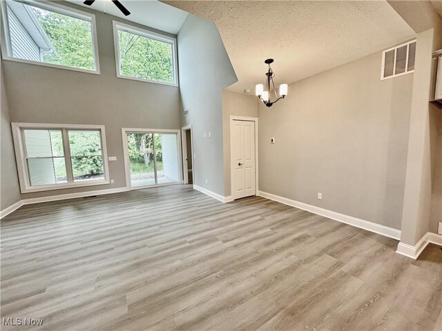 32054 Tuscan Ln Unit L-2, Avon Lake, OH 44012 - unfurnished living room with a chandelier, wood finished floors, a ceiling fan, a textured ceiling, and a high ceiling