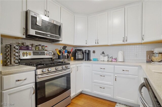 13 S River Rd, Munroe Falls, OH 44262 - kitchen with appliances with stainless steel finishes, white cabinetry, light countertops, backsplash, and light wood-style flooring