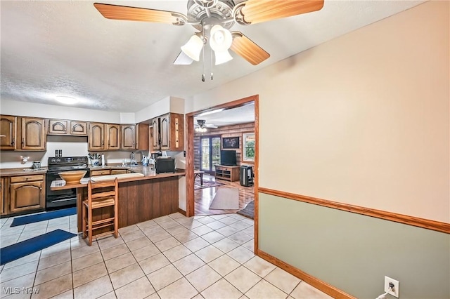 1683 Ridgewood Dr, Salem, OH 44460 - kitchen with black / electric stove, a ceiling fan, a peninsula, light tile patterned floors, and a breakfast bar