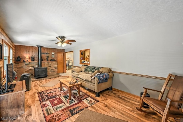 1683 Ridgewood Dr, Salem, OH 44460 - living room with a wood stove, ceiling fan, light wood-style flooring, wooden walls, and a textured ceiling