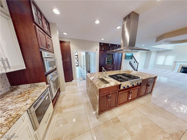 2474 Ginger Wren Rd, Pepper Pike, OH 44124 - kitchen featuring stainless steel gas cooktop, island range hood, a center island, light stone countertops, and a fireplace