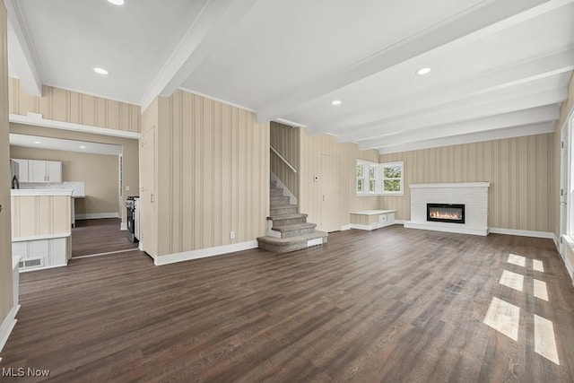 6434 Union Ave NE, Alliance, OH 44601 - unfurnished living room featuring beam ceiling, dark wood-type flooring, stairs, and a glass covered fireplace