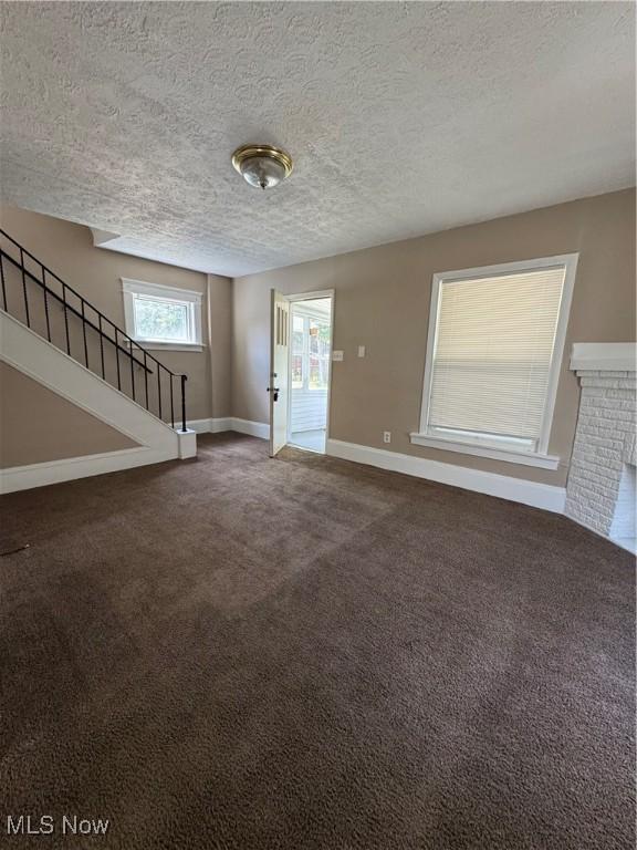 2239 23rd St SW, Akron, OH 44314 - unfurnished living room featuring dark colored carpet, stairs, and a textured ceiling