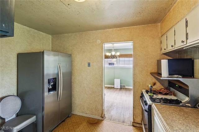 2992 Eldora Dr, Youngstown, OH 44511 - kitchen with stainless steel fridge, gas range oven, a chandelier, white cabinets, and light countertops