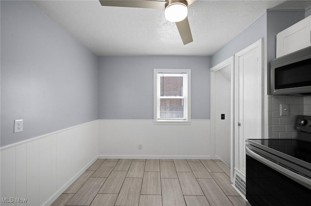 1835 Rockefeller Rd, Wickliffe, OH 44092 - kitchen featuring range with electric stovetop, stainless steel microwave, ceiling fan, backsplash, and a textured ceiling