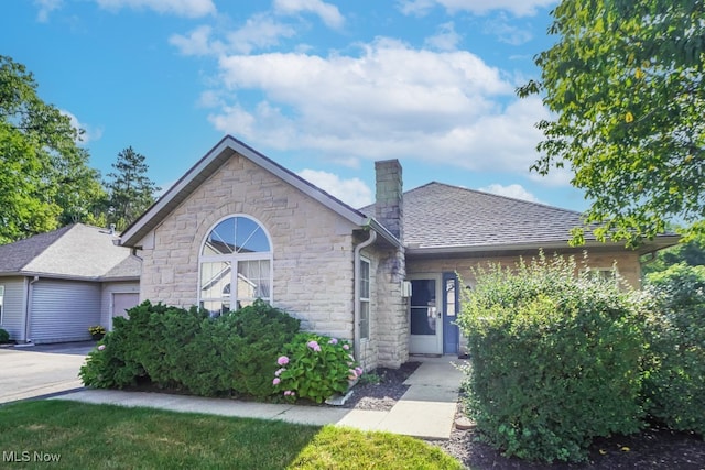 4039 Tannybrooke Ln NW Unit C, Canton, OH 44718 - view of front of house with stone siding, a chimney, a garage, a shingled roof, and driveway