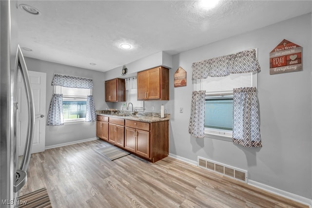 24850 Shoreview Ave, Euclid, OH 44123 - kitchen with freestanding refrigerator, light wood-style floors, brown cabinets, a textured ceiling, and light stone countertops