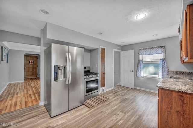 24850 Shoreview Ave, Euclid, OH 44123 - kitchen featuring appliances with stainless steel finishes, light wood-type flooring, brown cabinets, light stone counters, and a textured ceiling