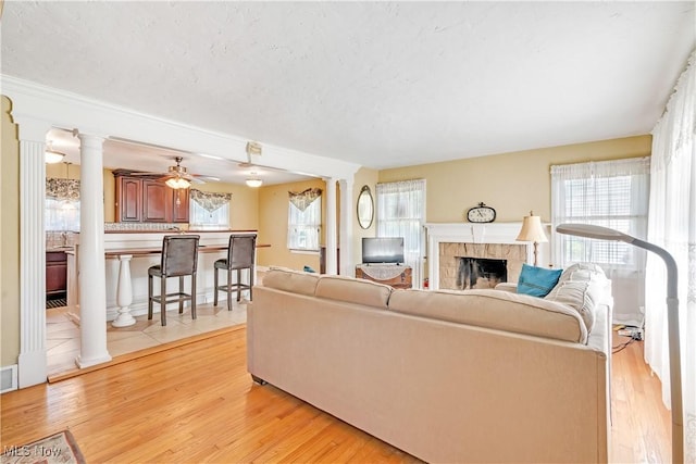 6100 Glenwood Ave, Boardman, OH 44512 - living area featuring ornate columns, a fireplace, light wood-type flooring, ceiling fan, and a textured ceiling
