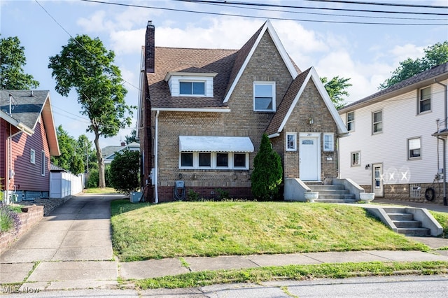 289 E Baird Ave, Barberton, OH 44203 - tudor house featuring brick siding, a chimney, a front lawn, a shingled roof, and driveway