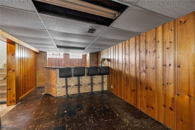 15617 Rockside Rd, Maple Heights, OH 44137 - below grade area with wood walls, a drop ceiling, a bar, stairway, and tile patterned floors