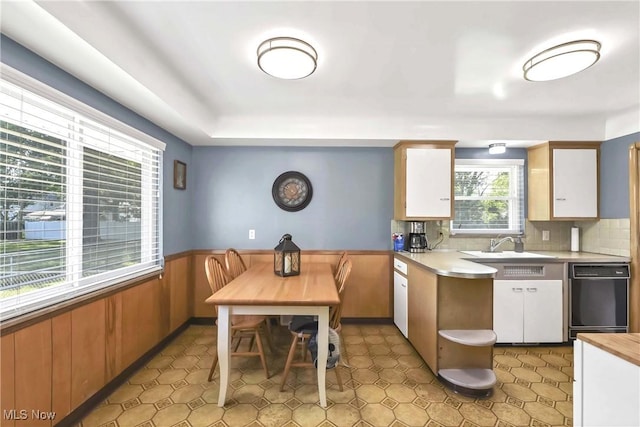 6713 Mackenzie Rd, North Olmsted, OH 44070 - kitchen with dishwasher, light countertops, white cabinetry, a wainscoted wall, and decorative backsplash