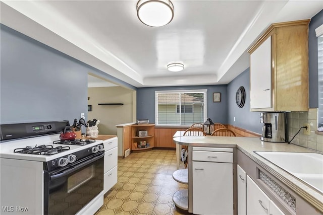 6713 Mackenzie Rd, North Olmsted, OH 44070 - kitchen with gas stove, a peninsula, light countertops, a tray ceiling, and white cabinets