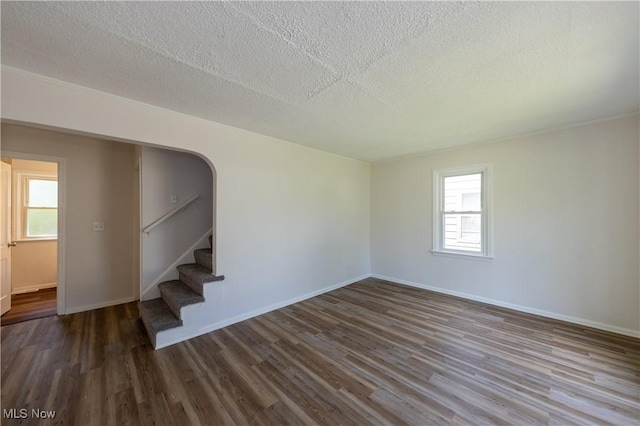21304 Watson Rd, Maple Heights, OH 44137 - unfurnished room with wood finished floors, stairs, plenty of natural light, a textured ceiling, and arched walkways