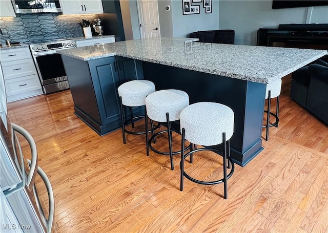 116 Ledgestone Ct, Berea, OH 44017 - kitchen featuring stainless steel stove, light wood-style flooring, white cabinets, a kitchen island, and backsplash