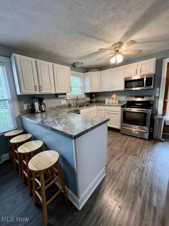 4575 Fishcreek Rd, Stow, OH 44224 - kitchen with stainless steel appliances, a peninsula, white cabinetry, dark wood-style floors, and a textured ceiling