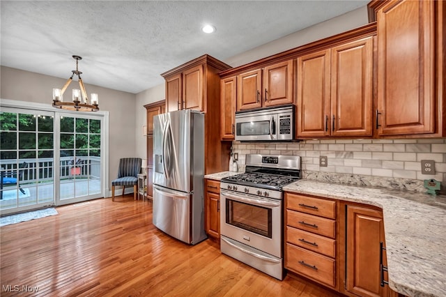 7955 Forest Valley Ln, Concord, OH 44077 - kitchen featuring appliances with stainless steel finishes, brown cabinets, light wood finished floors, backsplash, and a chandelier
