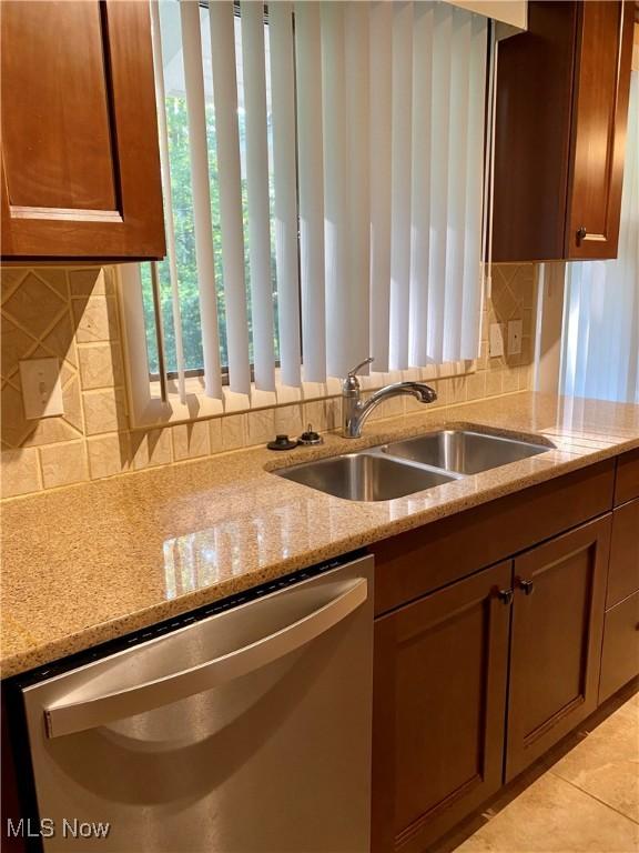 17079 Cats Den Rd, Chagrin Falls, OH 44023 - kitchen featuring stainless steel dishwasher, light stone counters, backsplash, light tile patterned floors, and brown cabinets