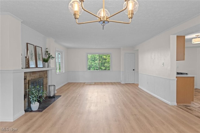 3695 S Hametown Rd, Norton, OH 44203 - unfurnished living room with light wood finished floors, a textured ceiling, a chandelier, wainscoting, and a stone fireplace