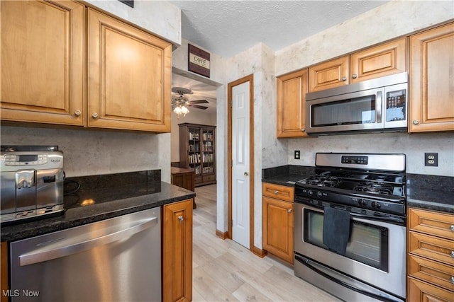 23730 Sawmill Bnd, Olmsted Falls, OH 44138 - kitchen featuring appliances with stainless steel finishes, light wood-style floors, a textured ceiling, ceiling fan, and dark stone countertops