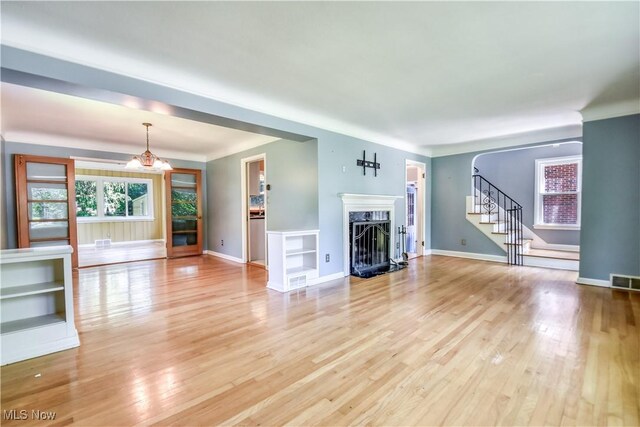2607 Ashurst Rd, University Heights, OH 44118 - unfurnished living room with stairs, light wood finished floors, a fireplace, and a chandelier