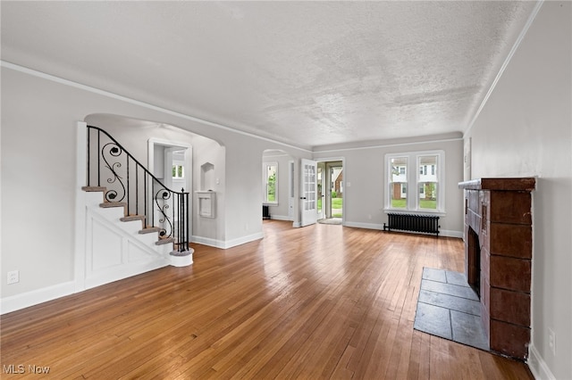 3497 Raymont Blvd, University Heights, OH 44118 - unfurnished living room featuring radiator, arched walkways, a fireplace with flush hearth, light wood finished floors, and crown molding