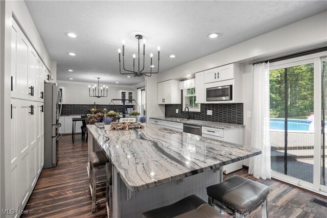 26938 Tall Oaks Trl, Olmsted Twp, OH 44138 - kitchen featuring stainless steel appliances, dark wood-style floors, a chandelier, decorative backsplash, and white cabinetry