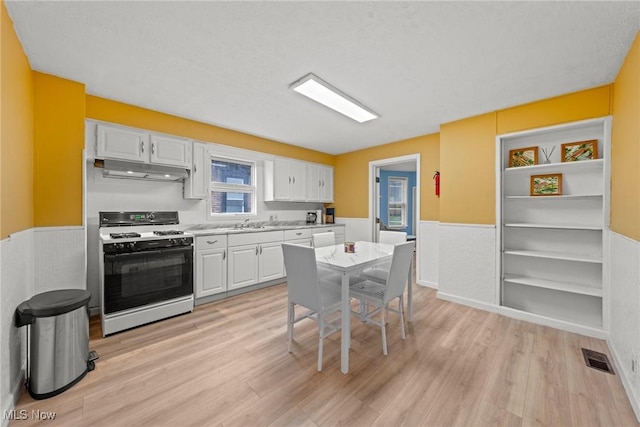 1411 E 47th St, Cleveland, OH 44103 - kitchen with white gas range, under cabinet range hood, a wainscoted wall, light wood-style floors, and white cabinetry
