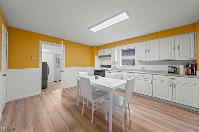 1411 E 47th St, Cleveland, OH 44103 - kitchen featuring gas range, a wainscoted wall, light countertops, white cabinets, and washer / clothes dryer