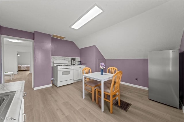 1411 E 47th St, Cleveland, OH 44103 - kitchen featuring white range with gas cooktop, stainless steel refrigerator, light wood-style floors, lofted ceiling, and light countertops