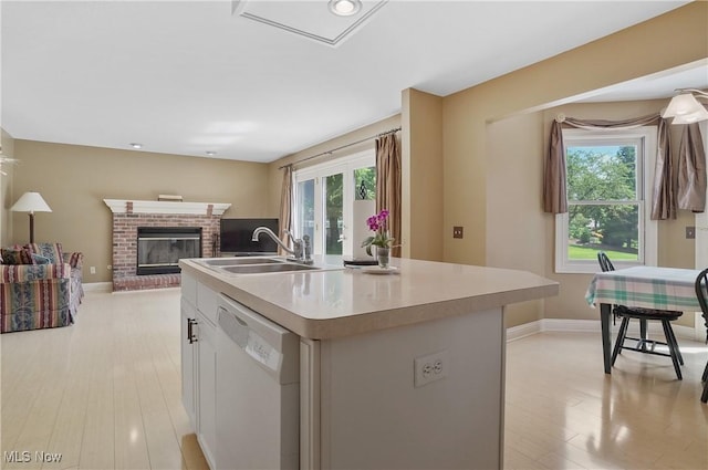 8883 Michaels Ln, Broadview Heights, OH 44147 - kitchen featuring white dishwasher, a center island with sink, light countertops, light wood-style flooring, and a brick fireplace