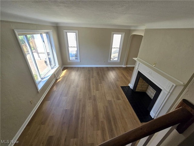 26313 Oriole Ave, Euclid, OH 44132 - unfurnished living room with a fireplace with flush hearth, a textured ceiling, wood finished floors, arched walkways, and a textured wall