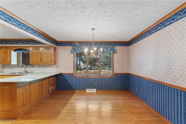 120 Vineyard Way, Doylestown, OH 44230 - kitchen with light wood finished floors, ornamental molding, a chandelier, brown cabinetry, and wallpapered walls