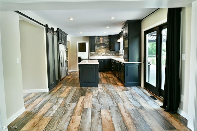 191 Maple Leaf Dr, Hubbard, OH 44425 - kitchen featuring a barn door, wall chimney range hood, light countertops, light wood-style floors, and a kitchen island